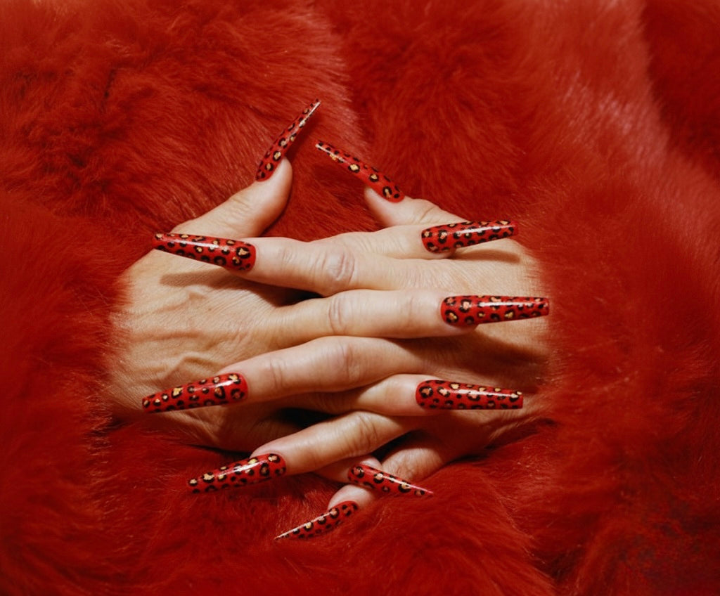 Long red leopard print press on nails on hands resting on luxurious red faux fur pointed stiletto shape high fashion nail art