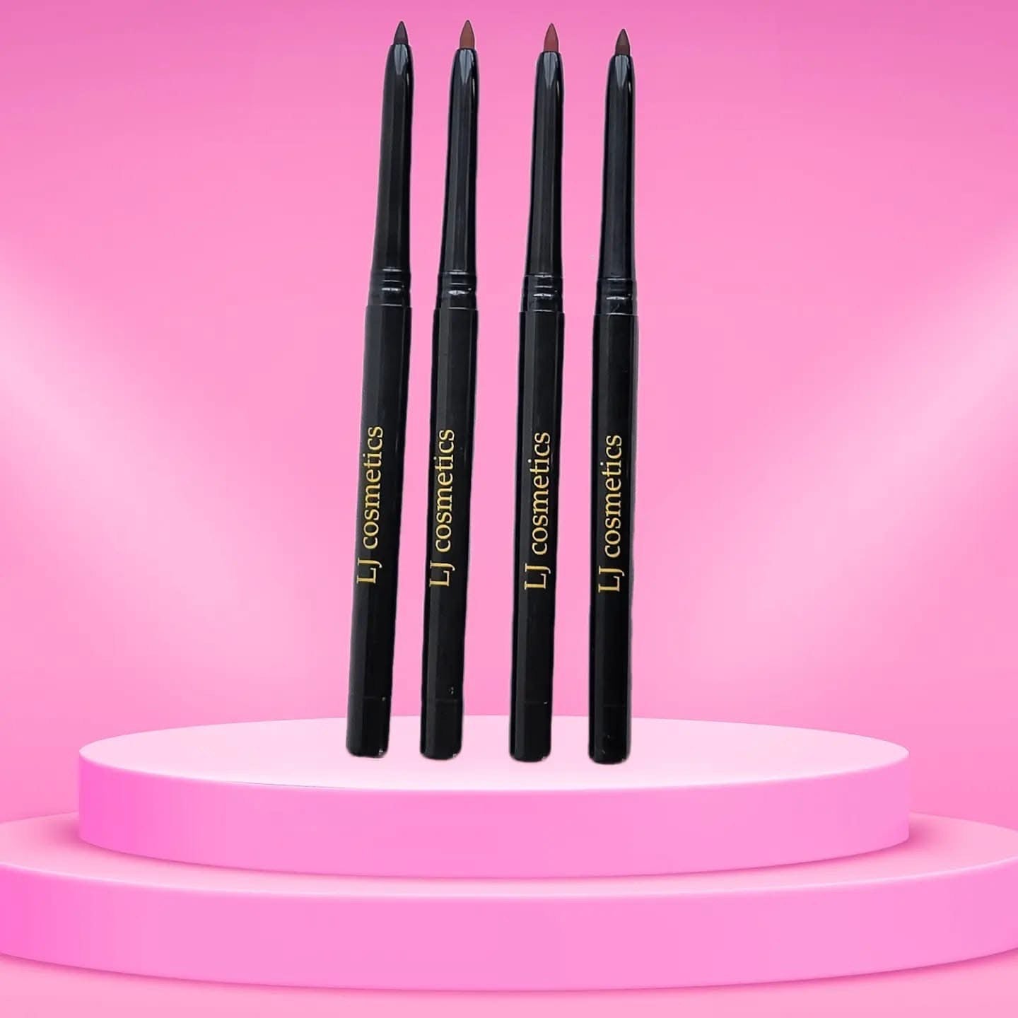 Four black cosmetic pencils with gold text on a pink platform and background