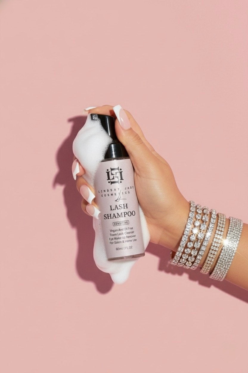 Hand holding a bottle of Lash Shampoo against a pink background