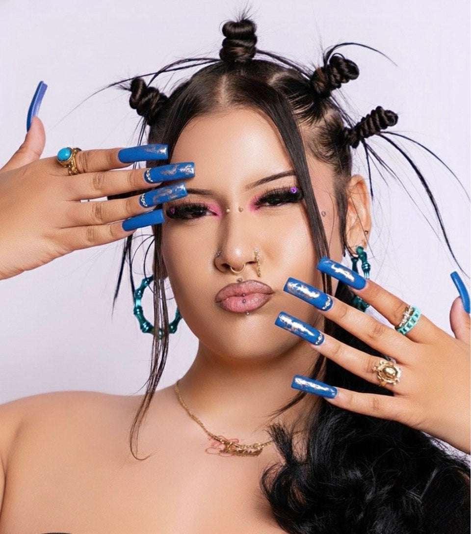Woman with styled hair and blue nail press on nails with silver design and bling posing against a light background