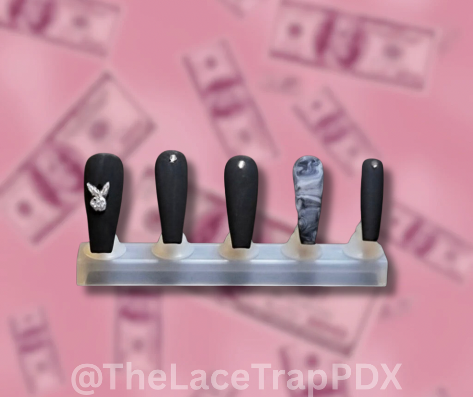 Set of five black and one marble-patterned and playboy bunny charm press on nails on a clear stand against a pink background with blurred text.