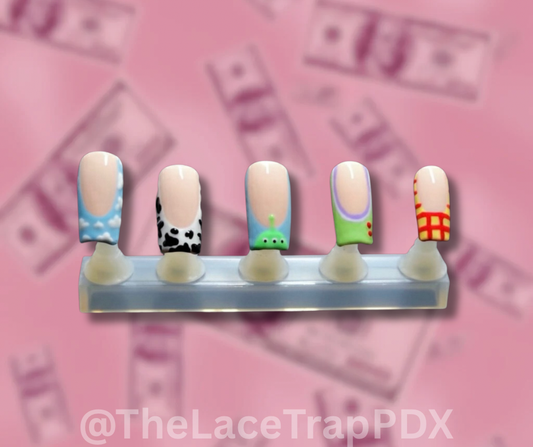 Set of colorful toy story inspired nail art on press on nails on a stand with a pink background featuring dollar bills.